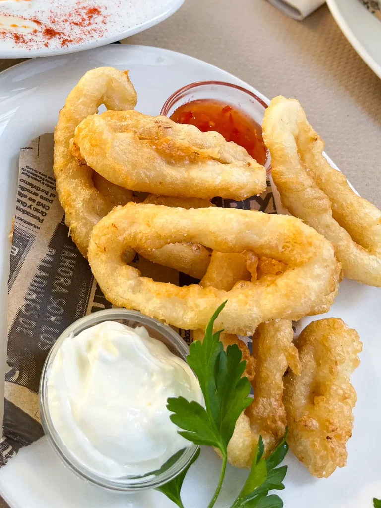 Calamares fritos — golden battered squid rings and strips with aioli and sweet chilli sauce on a newspaper-lined plate, León