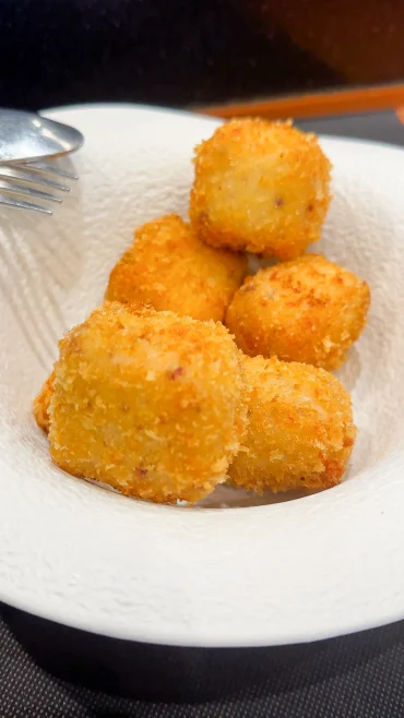 Croquetas de jamón — five round golden-fried croquettes with coarse breadcrumb crust on a white textured plate, Asturias
