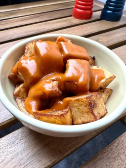 Patatas bravas — chunky fried potato cubes drenched in thick glossy bravas sauce in a white ceramic bowl, Madrid