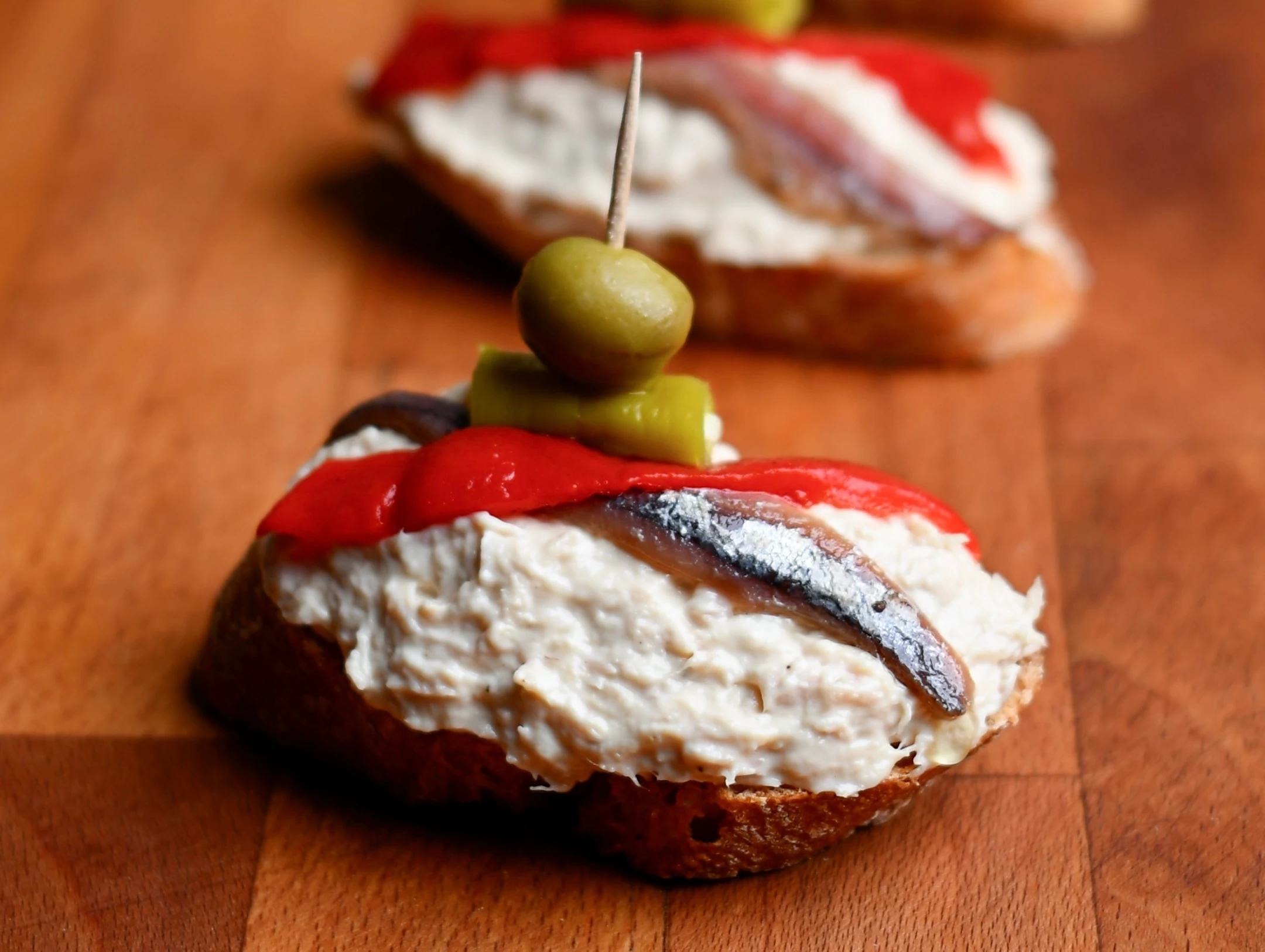 Pintxo de bonito — close-up of tuna spread, anchovy, roasted red pepper and olive on a toothpick on a baguette slice, Basque Country