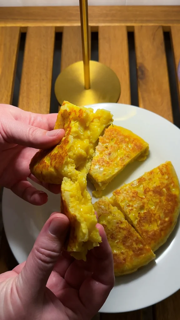 Tortilla de patatas — hands pulling apart a cuajada slice revealing a soft runny interior, with wedges on a white plate, Valencia