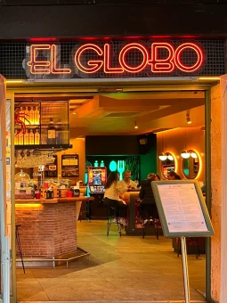 El Globo pintxo bar — red neon sign above an open entrance with a warm-lit interior, brick bar counter and menu board outside, Bilbao