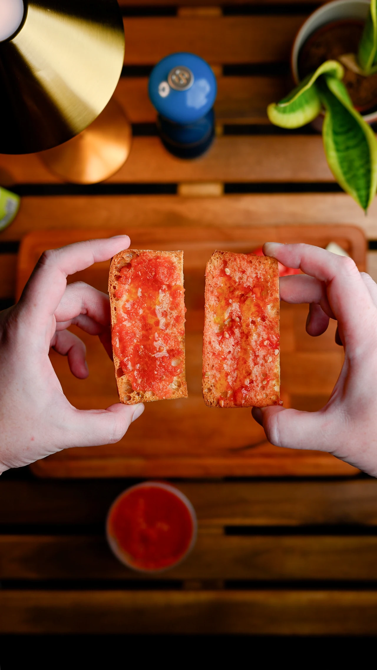 Pan con tomate — two slices of toasted bread rubbed with fresh tomato, held up by two hands over a wooden board