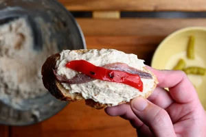 Pintxo de bonito recipe step 7 — a strip of roasted red pepper laid over the anchovy on bonito mayo spread on a baguette slice