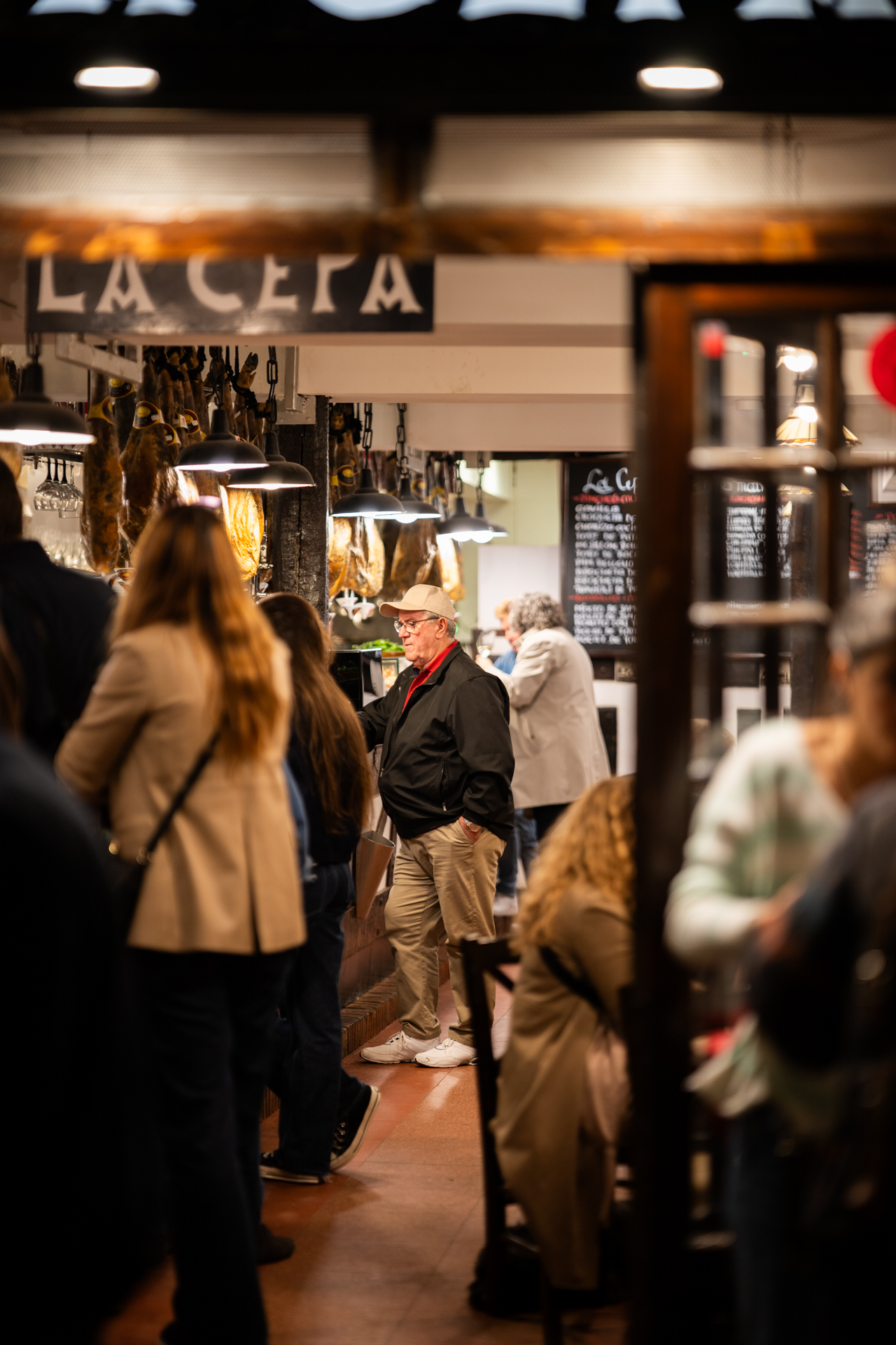 La Cepa bar entrance with illuminated sign above a warm crowded interior and hanging jamón, San Sebastián, Spain
