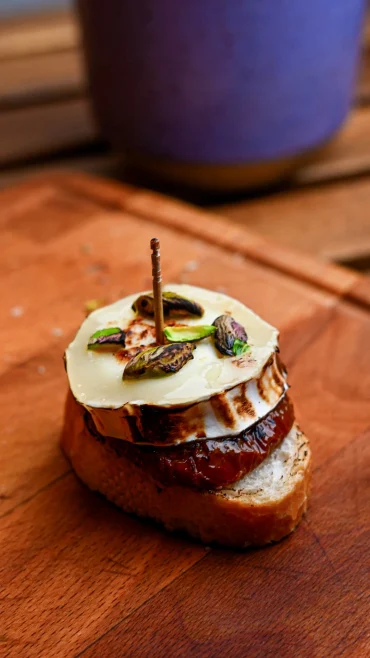 Pintxo de queso de cabra recipe — charred goat's cheese and dried tomato on toasted baguette with pistachios and a toothpick, Basque Country