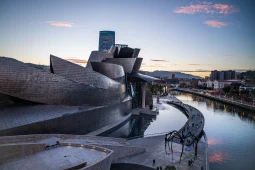 Guggenheim Museum Bilbao titanium facade with Maman spider sculpture and Nervión river at dusk, Bilbao, Spain