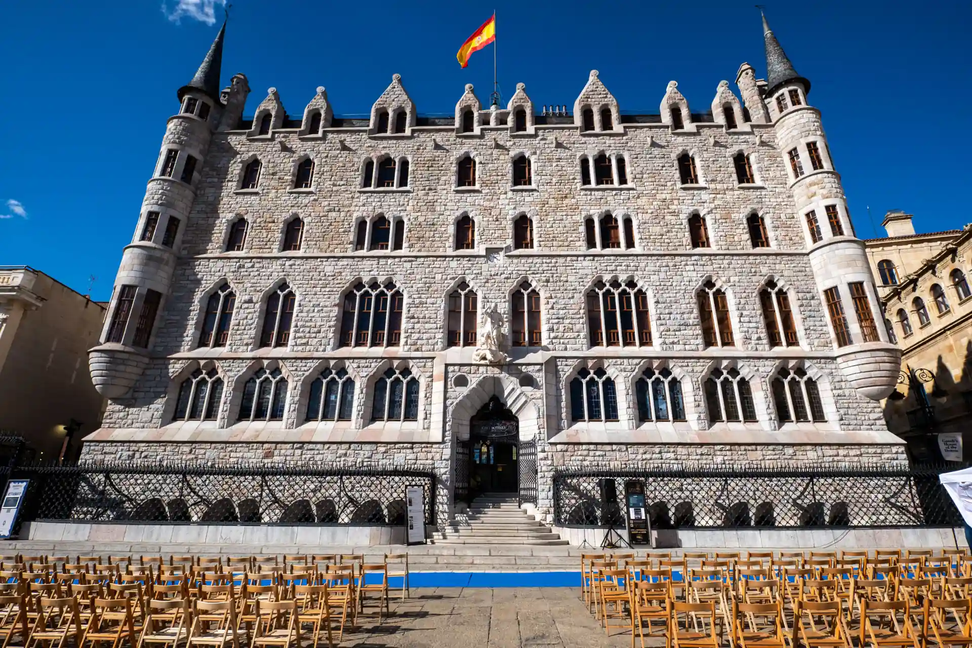 Palacio de los Guzmanes Gothic-Renaissance stone facade with Spanish flag and rows of chairs in the square, León, Spain