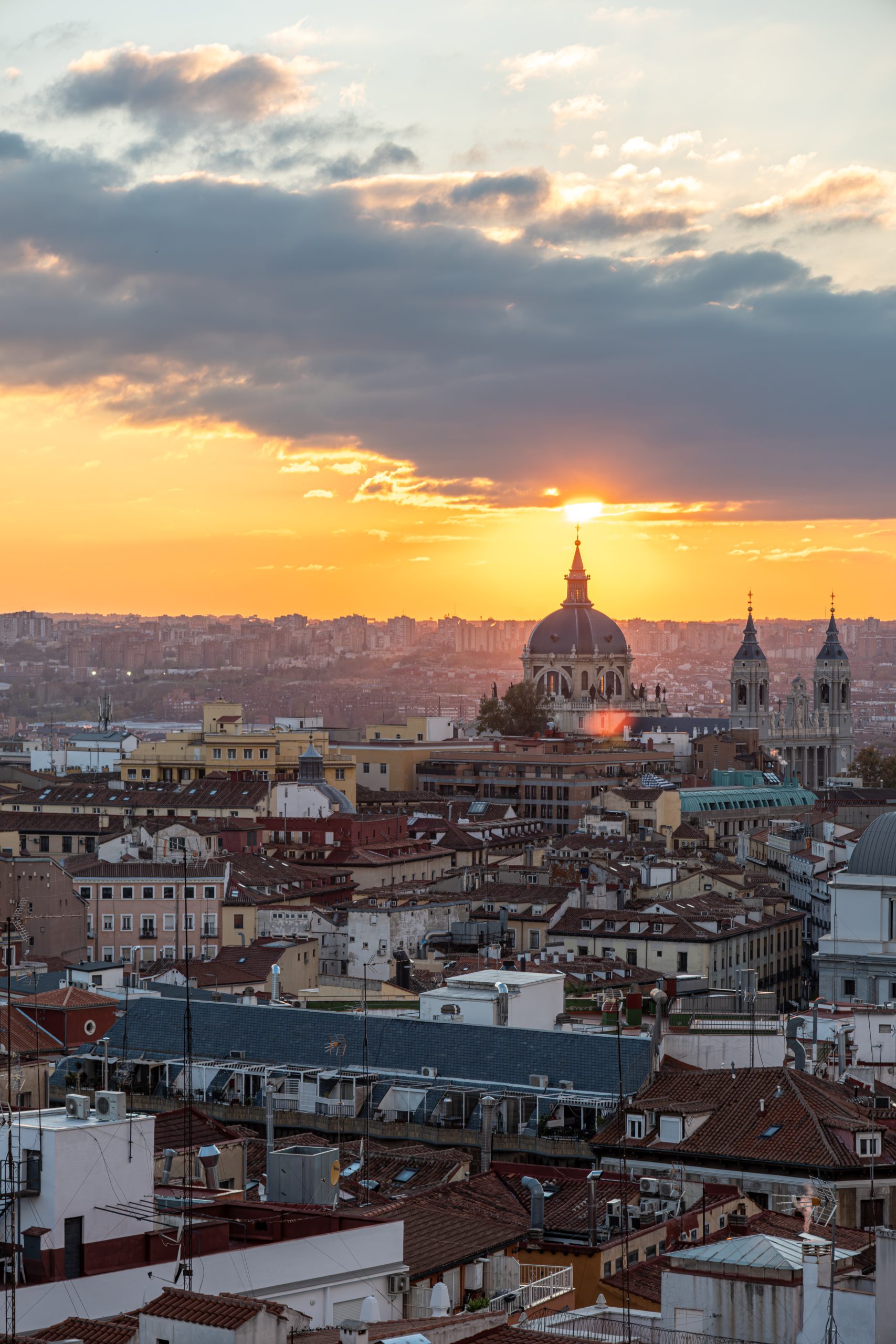 Madrid skyline at sunset — Almudena Cathedral dome and spired towers above a dense roofscape of terracotta tiles and TV aerials, Spain
