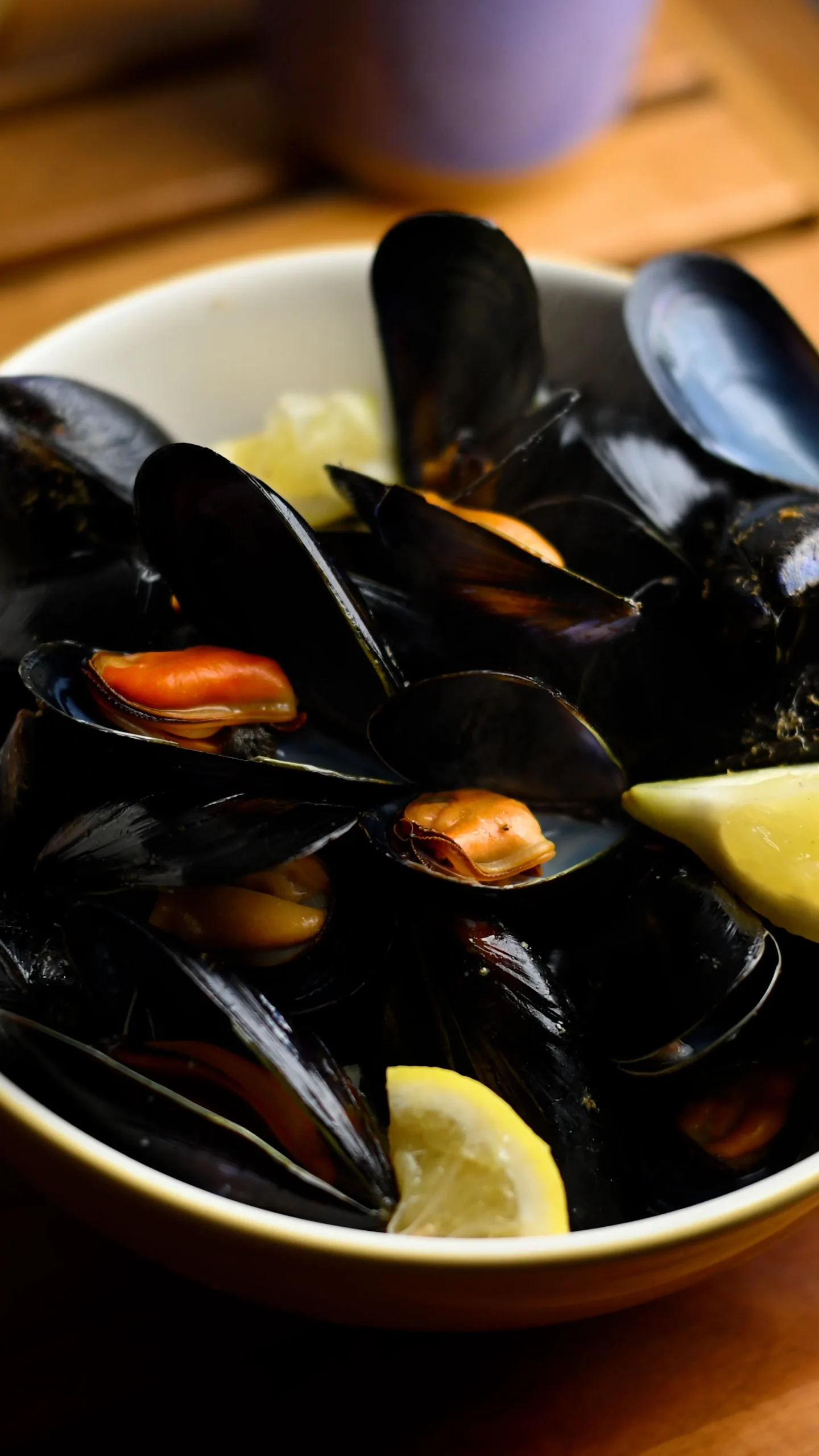 Mejillones al vapor — steamed mussels with orange flesh in a cream bowl, two lemon wedges tucked between the open black shells