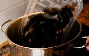 Mejillones al vapor step 1 — cleaned mussels being tipped from a plastic container into a steaming stainless steel pot on a hob