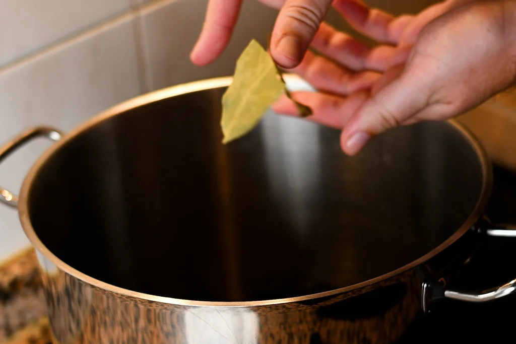 Mejillones al vapor step 2 — hands crushing a bay leaf over an empty stainless steel pot on a ceramic hob