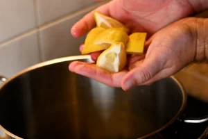 Mejillones al vapor step 6 — hands holding lemon wedges over a stainless steel pot on a hob, about to add them to the steam