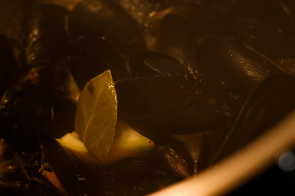 Mejillones al vapor step 7 — mussels opening in a steaming pot with a bay leaf and lemon wedge visible inside