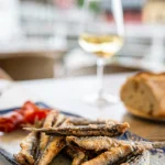 Parrochas fritas — small whole fried fish with roasted red pepper on a blue-rimmed plate, with bread and white wine, Llanes