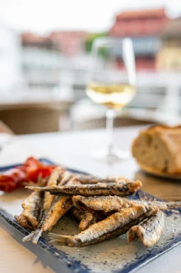 Parrochas fritas — small whole fried fish with roasted red pepper on a blue-rimmed plate, with bread and white wine, Llanes