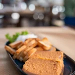 Pastel de cabracho - a dense orange fish pâté wedge with toasted bread slices on a dark oval plate at Sidrería La Casona, Llanes
