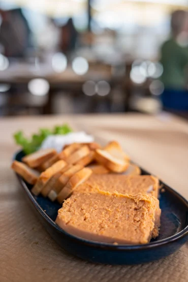 Pastel de cabracho - a dense orange fish pâté wedge with toasted bread slices on a dark oval plate at Sidrería La Casona, Llanes