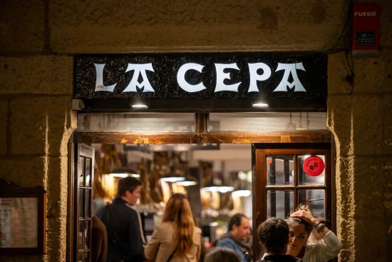 La Cepa bar entrance with illuminated sign above a warm crowded interior and hanging jamón, San Sebastián, Spain
