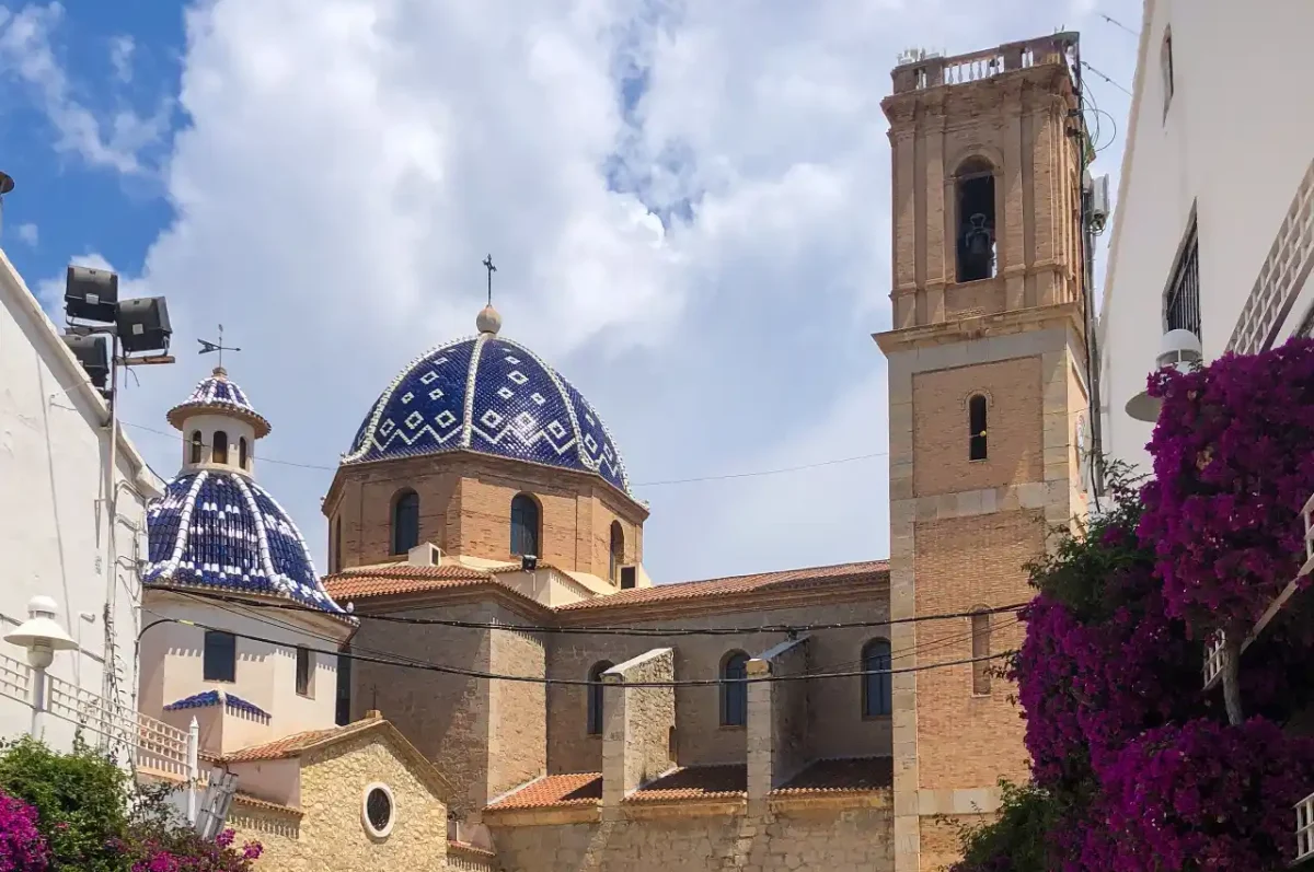 Altea old town plaza — church with a blue and white tiled dome and square bell tower, framed by purple bougainvillea, Alicante