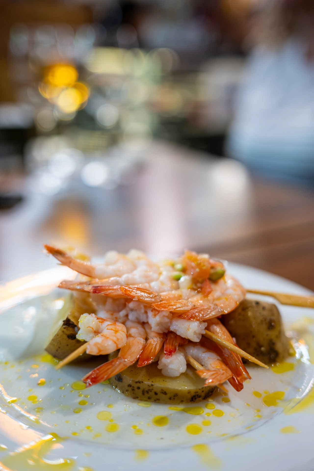 Skewered langoustines layered over sliced potatoes drizzled with oil on a white plate at Chantarela, Spain.