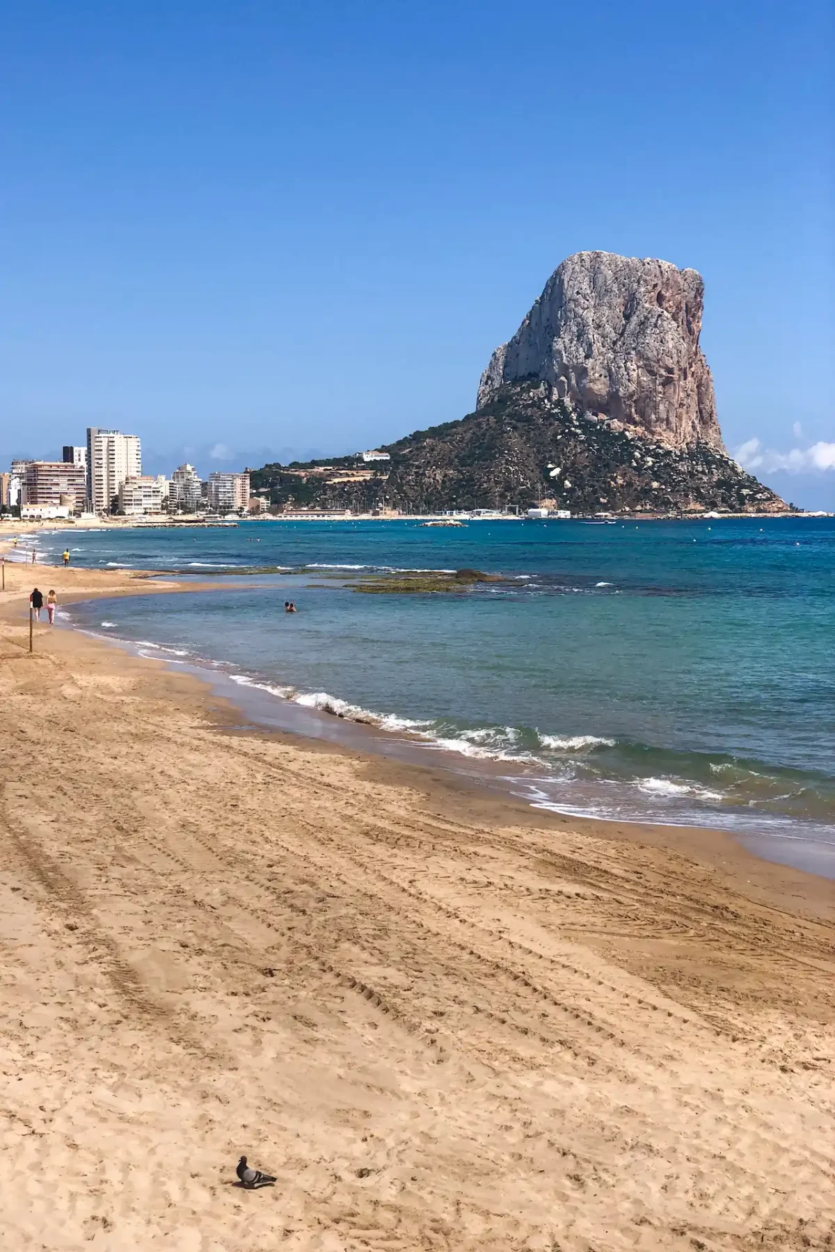 Calpe beach - wide sandy shore with the Peñón de Ifach limestone rock rising from the sea, turquoise water and a clear blue sky