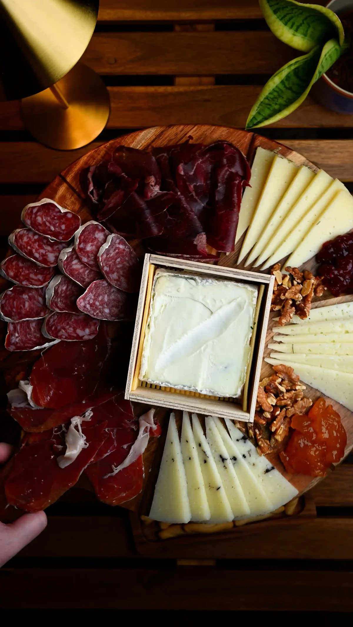 Spanish charcuterie board — cured meats, salami, three cheeses, soft cheese in a box, walnuts and jam on a round wooden board, Spain