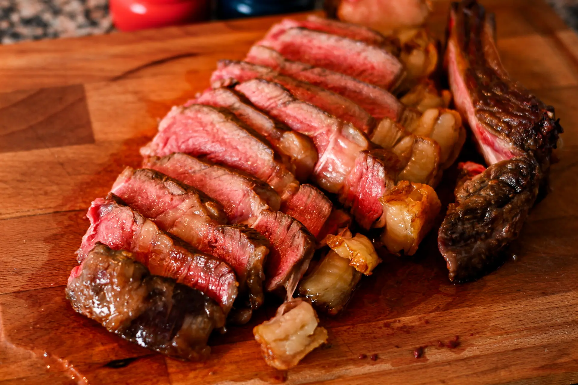 A sliced medium-rare chuleton steak with a charred crust on a wooden cutting board, Spain.