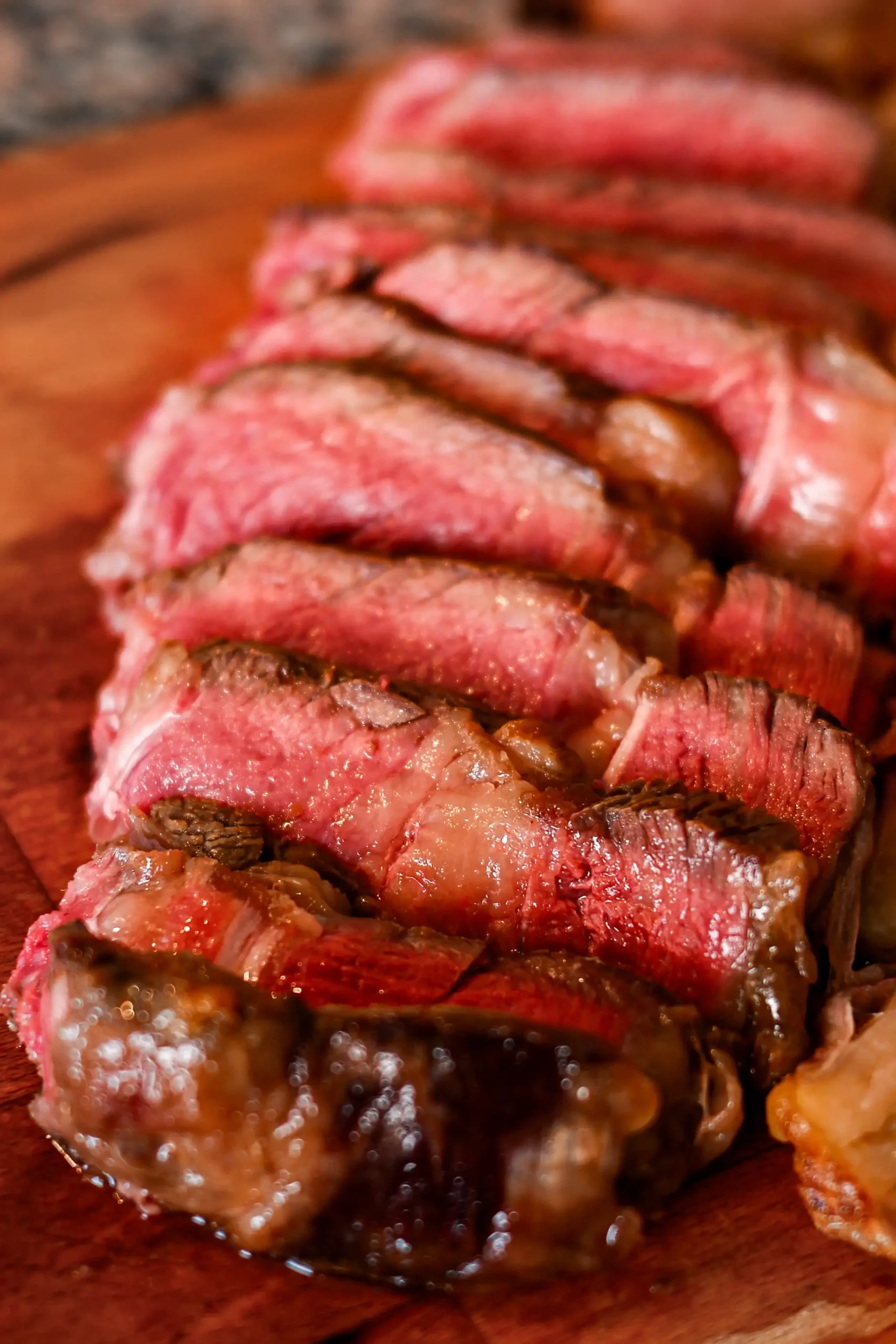 Sliced medium-rare chuleton steak showing a pink center and charred crust on a wooden board, Spain.
