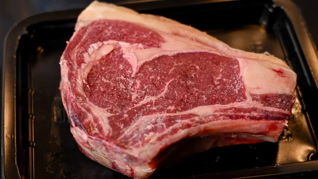 A raw, thick-cut chuleton steak resting in a black tray before cooking, Spain.