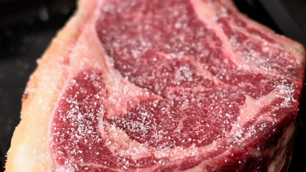 Coarse sea salt sprinkled evenly over the surface of a raw chuleton steak, Spain.