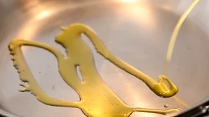 Golden olive oil being poured into a hot stainless steel pan, Spain.
