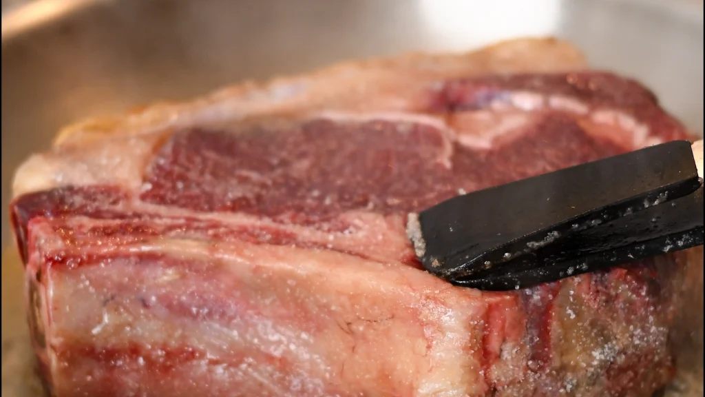 Tongs holding a thick chuleton steak as it sears on its first side in a hot pan, Spain.