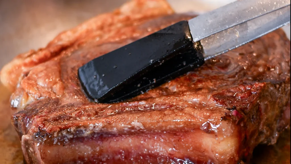 Tongs pressing down on a seared chuleton steak in a pan, Spain.