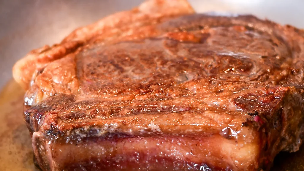 A well-seared chuleton steak resting in a pan as it finishes cooking on its second side, Spain.