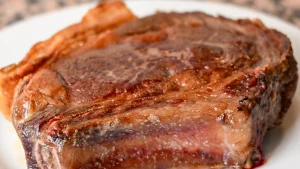 A cooked, whole chuleton steak resting on a white plate after searing, Spain.