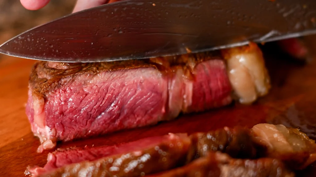 A knife slicing into a juicy, medium-rare chuleton steak on a wooden board, Spain.