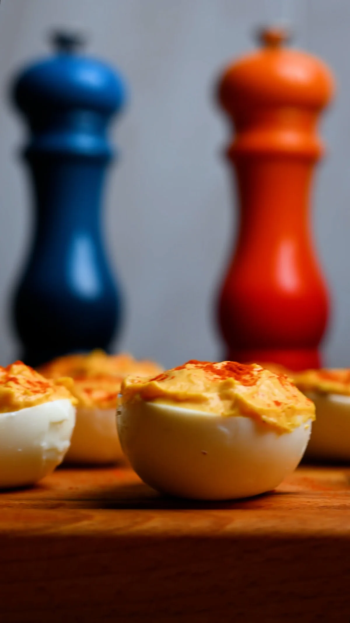 Huevos rellenos — boiled egg halves filled with paprika-spiced yolk mixture on a wooden board, with blue and orange pepper mills behind, Spain