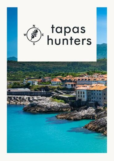 Tapas Hunters Issue 03 cover — Llanes harbour with turquoise water, rocky coastline and orange-roofed town, Asturias, Spain