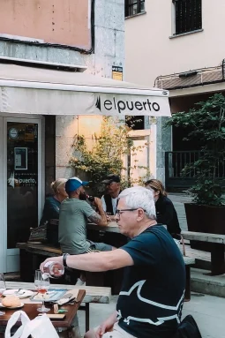 Sidrería Restaurante El Puerto terrace — diners at wooden tables under a white awning on a pedestrian street, Llanes, Asturias