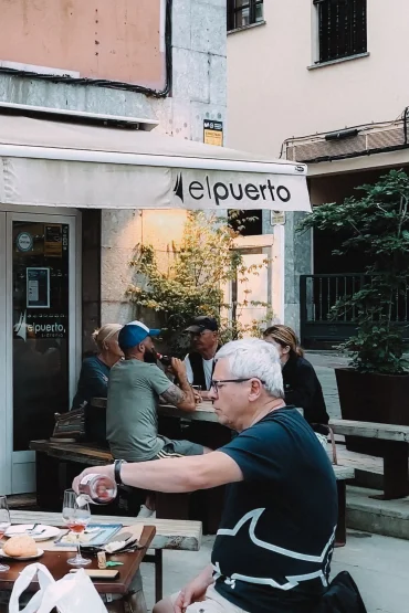 Sidrería Restaurante El Puerto terrace — diners at wooden tables under a white awning on a pedestrian street, Llanes, Asturias