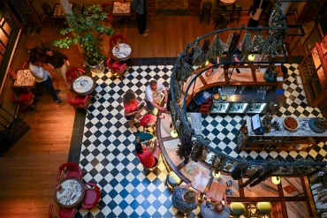 Spanish bar interior from above — black and white diamond floor tiles, red chairs, a curved bar counter and dried herbs hanging overhead
