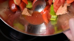 Close-up of a stainless steel bowl showing tomato juices gathering at the bottom among chopped vegetables and bread pieces.