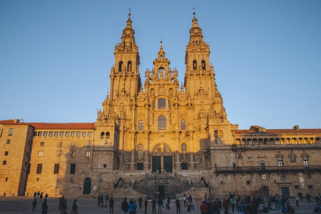 The grand stone facade of the Cathedral of Santiago de Compostela with twin bell towers glowing in the golden evening light, Santiago de Compostela.