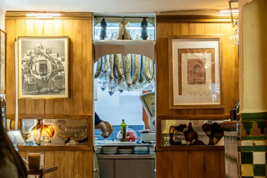 The cozy wooden interior of La Trastienda showing framed artwork, wood paneling, and a view into the back counter where cured meats hang in Granada, Spain.