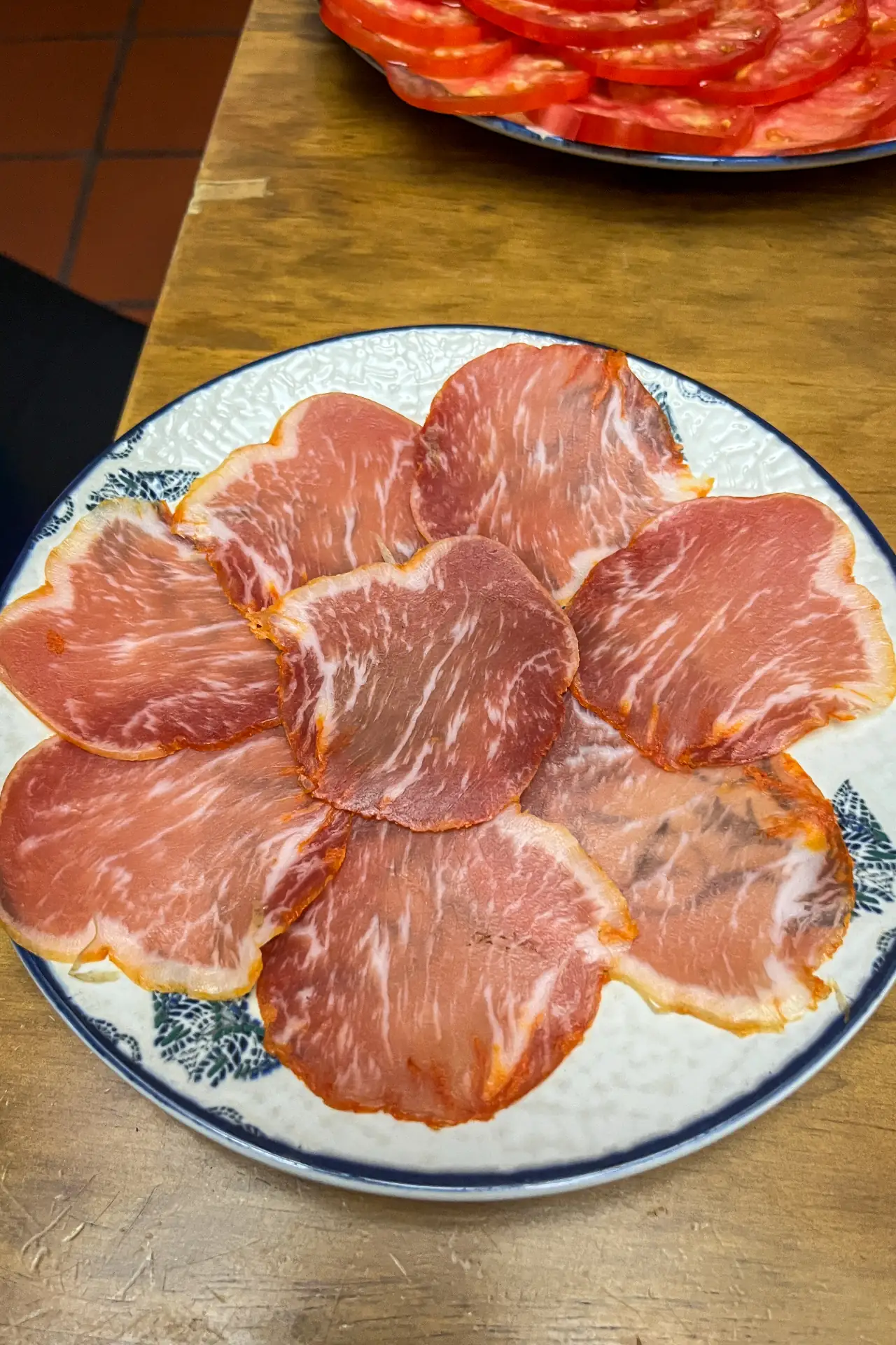 Lomo ibérico de bellota — thin-sliced cured pork loin fanned on a blue-rimmed ceramic plate, sliced tomatoes on a second plate behind, La Trastienda, Granada