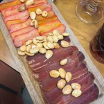 Slices of cured mojama and huevas de maruca garnished with roasted almonds on a wooden serving board at La Trastienda, Granada.