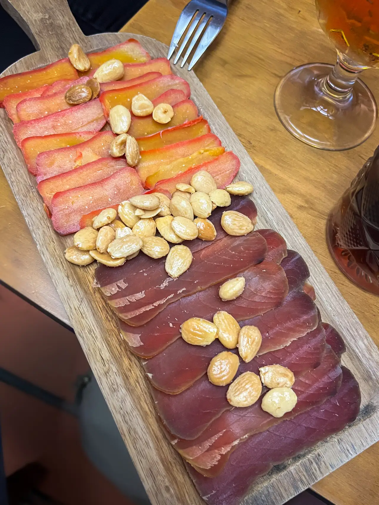 Slices of cured mojama and huevas de maruca garnished with roasted almonds on a wooden serving board at La Trastienda, Granada.