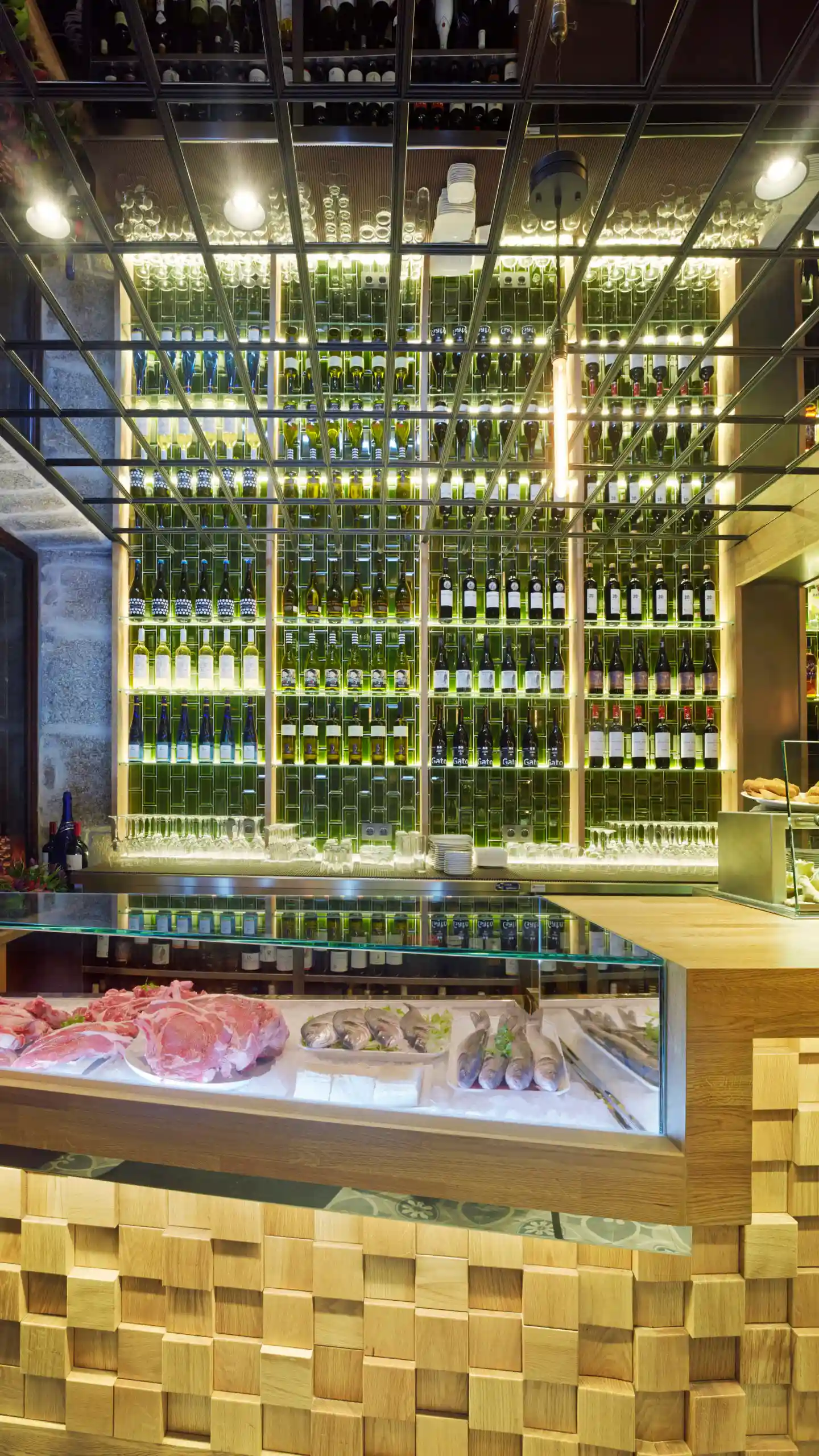 Papatorio restaurant interior — fresh fish and meat display counter with a backlit floor-to-ceiling wine wall, Santiago de Compostela, Spain