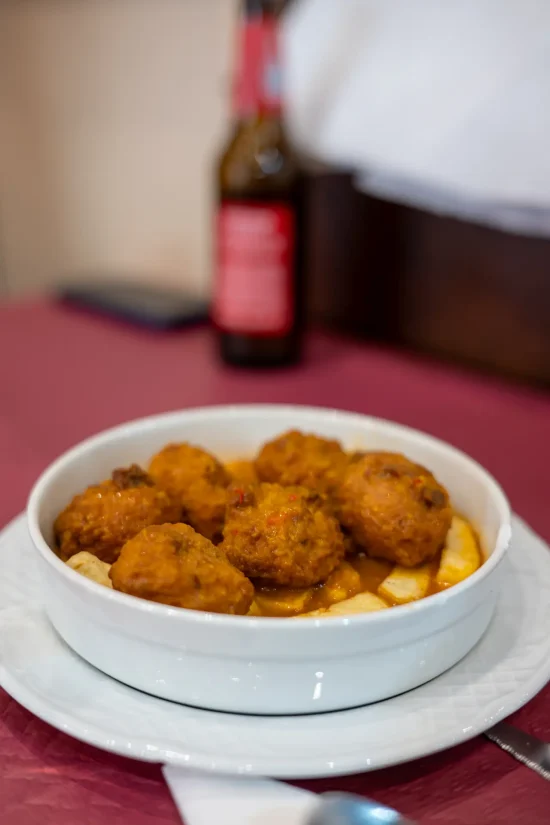 Close-up of homemade cuttlefish meatballs (albóndigas de choco) served in a savory sauce with fries in a white bowl at Sol y Sombra in Seville, Spain.